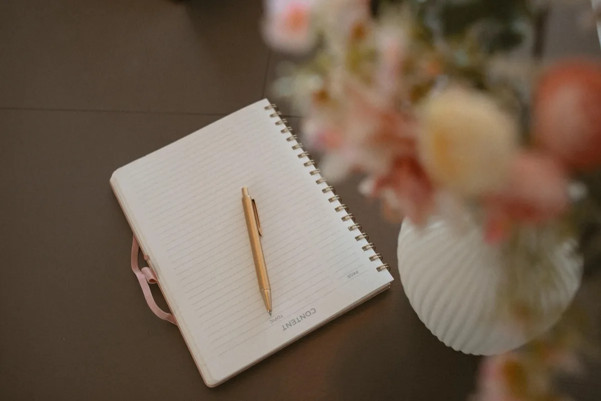 A notebook, gold pen, and florals from the Anchor & Bloom brand world