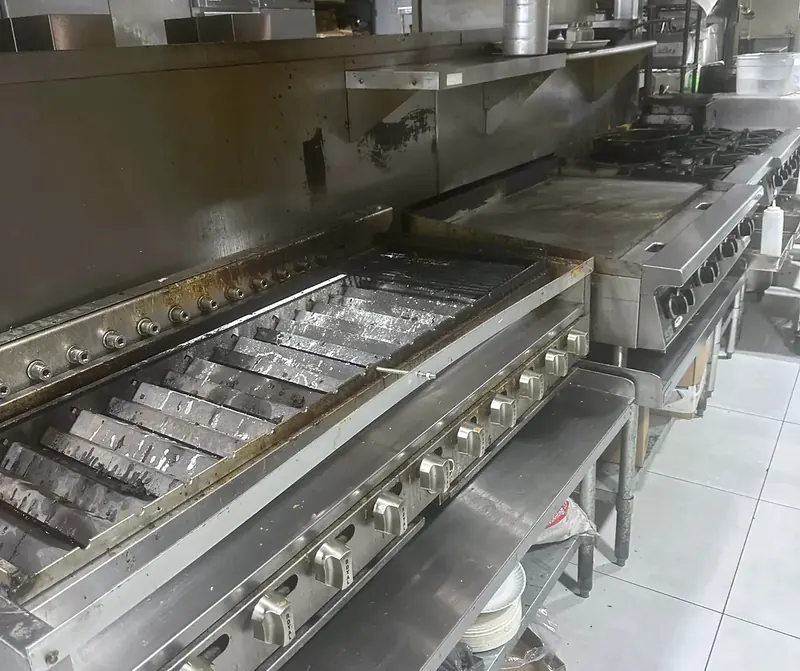 Stainless-steel charbroilers and griddle in a cooking line beneath a commercial exhaust hood